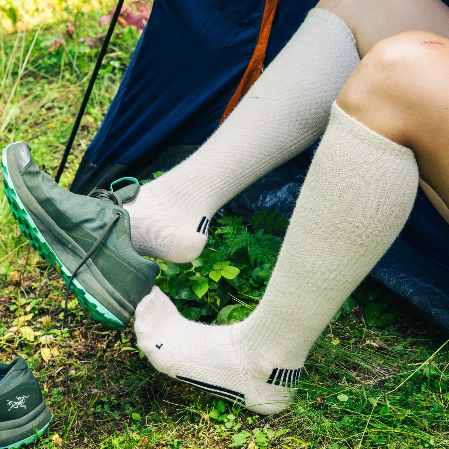 Person wearing green shoes and white knee-high socks sitting on grass